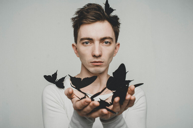 Person hält schwarze Schmetterlinge in den Händen vor neutralem Hintergrund – Symbol für Transformation und neuronale Plastizität.