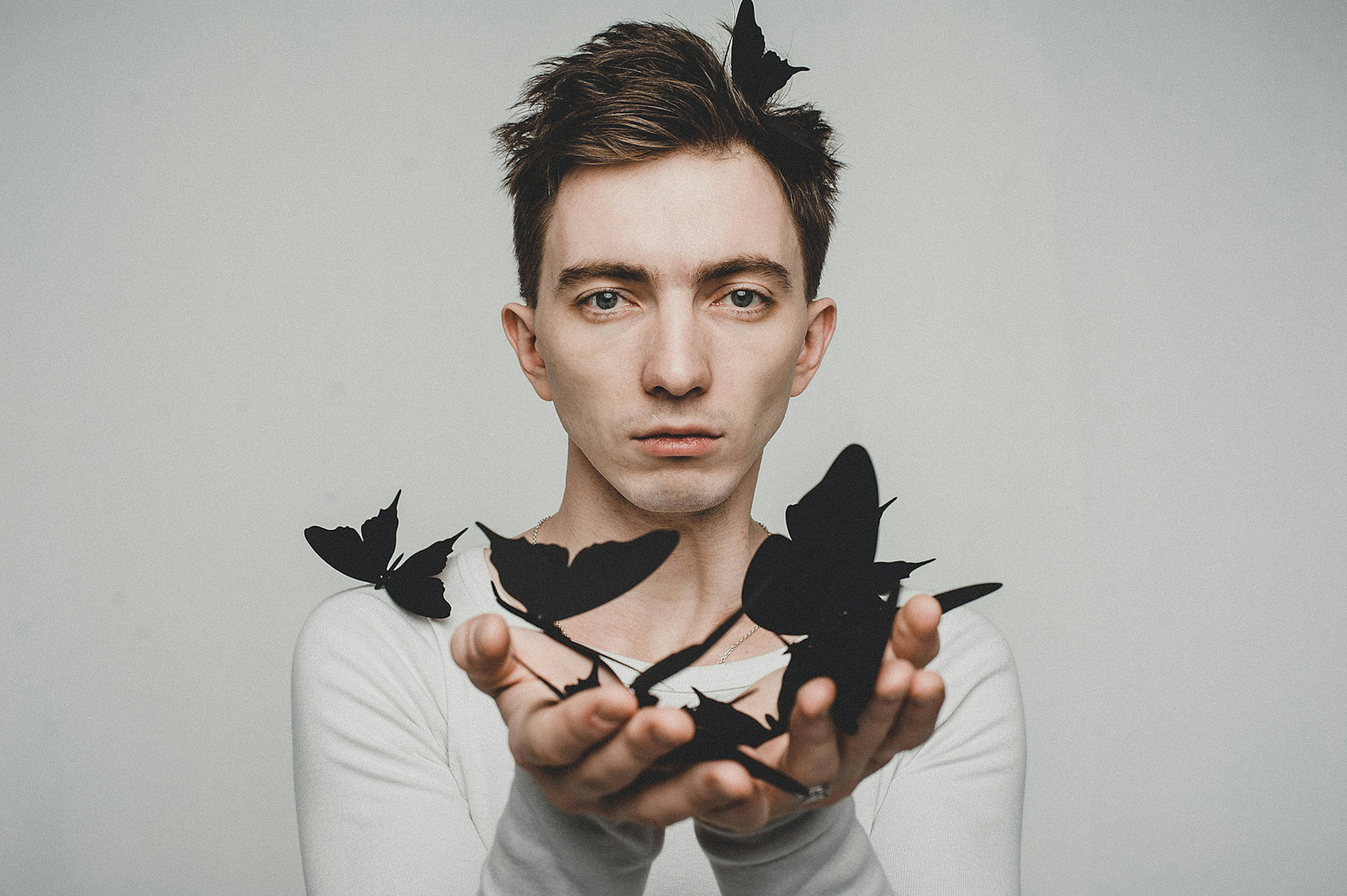 Person hält schwarze Schmetterlinge in den Händen vor neutralem Hintergrund – Symbol für Transformation und neuronale Plastizität.