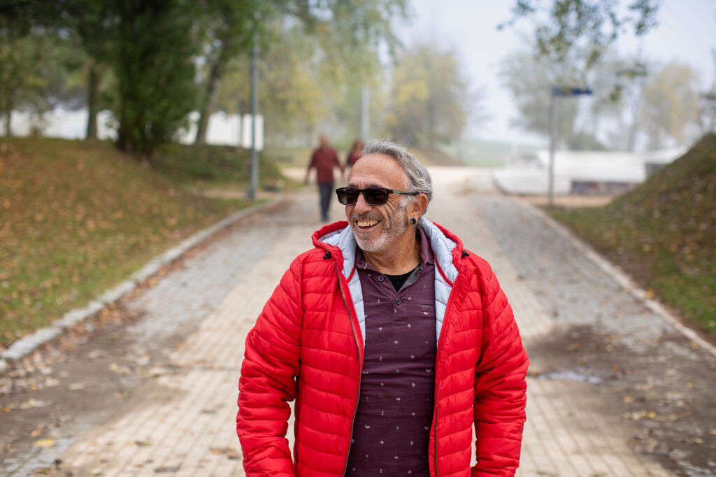 Älterer Mann mit roter Jacke spaziert entspannt auf einem Weg im Park – Symbolbild für ein aktives Leben mit HIV.