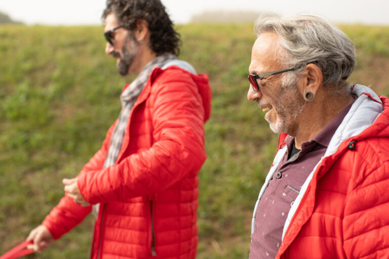 HIV-Status: Zwei Männer mit roten Jacken gehen gemeinsam durch eine Landschaft – Symbolbild für Unterstützung und Lebensqualität von Menschen mit HIV.