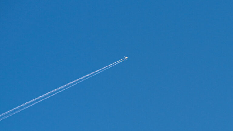 Flugzeug mit Kondensstreifen am blauen Himmel als Symbol für Freiheit, Distanz und Intimität in Beziehungen.