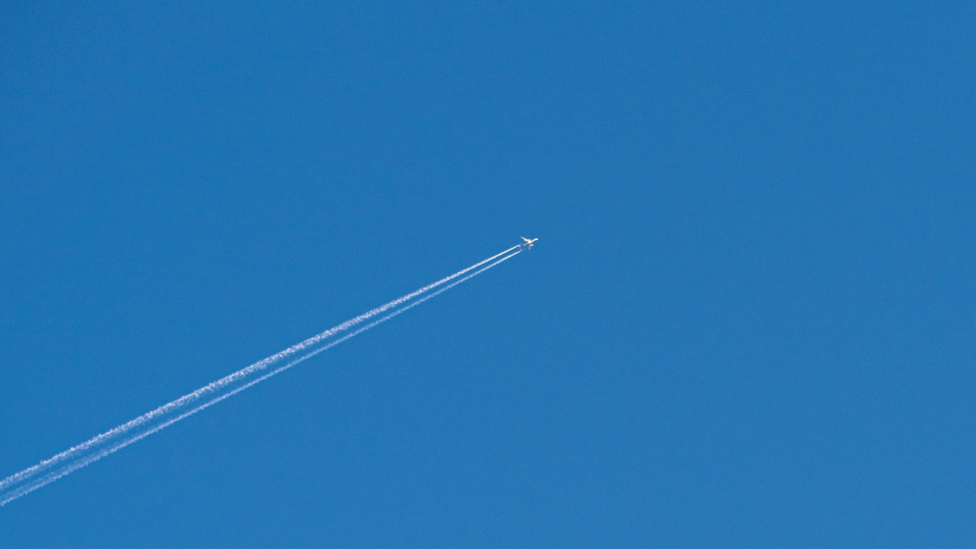 Flugzeug mit Kondensstreifen am blauen Himmel als Symbol für Freiheit, Distanz und Intimität in Beziehungen.