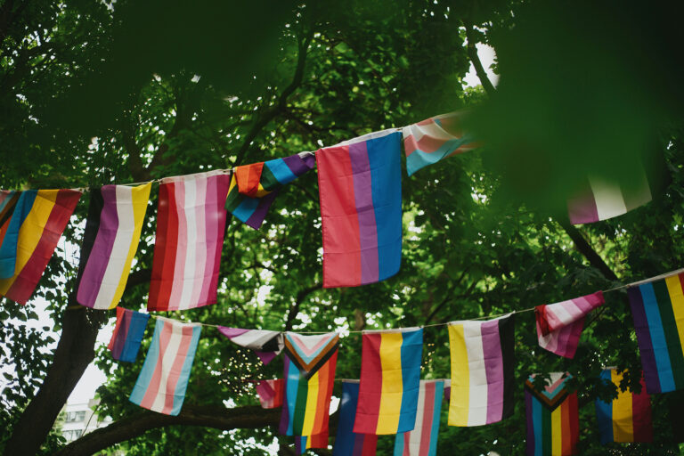 Bunte Pride-Flaggen hängen zwischen grünen Bäumen